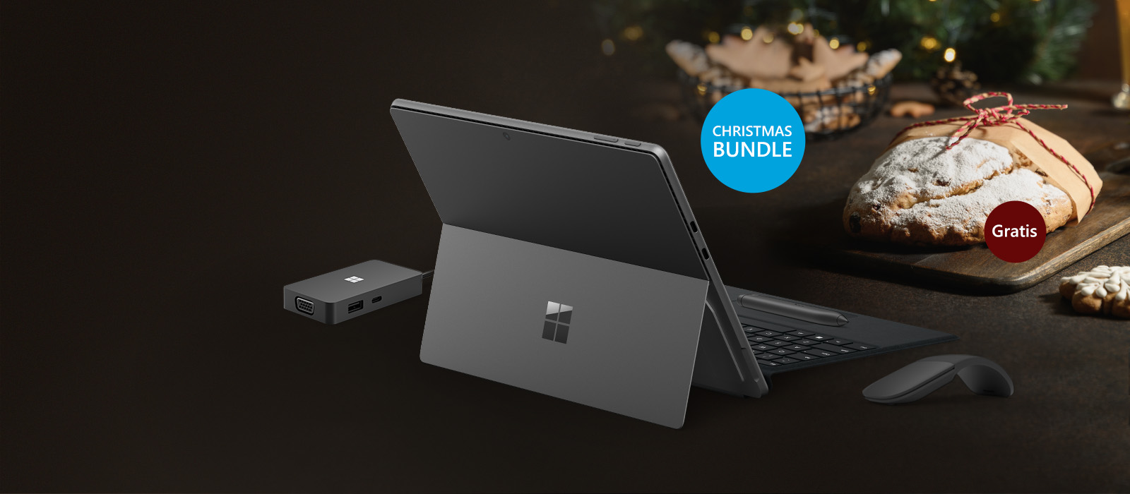 Surface Pro 9 inklusive Surface Arc Mouse, Surface Signature Keyboard mit Slim Pen 2 und Microsoft USB-C Travel Hub sind vor einem weihnachtlichen Hintergrund und einem Stollen dargestellt 