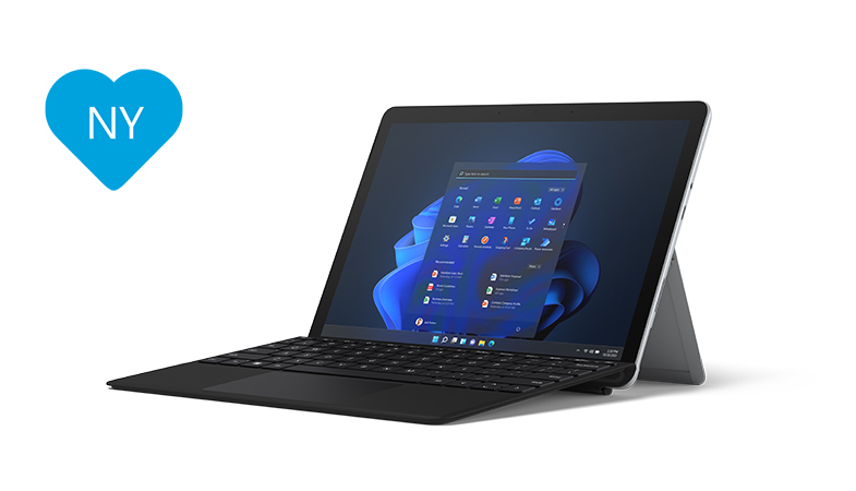 Surface Go 3 i platin med sort Type Cover i laptoptilstand set i et sideperspektiv med et blåt hjerte til venstre for Surface, hvorpå der står NY