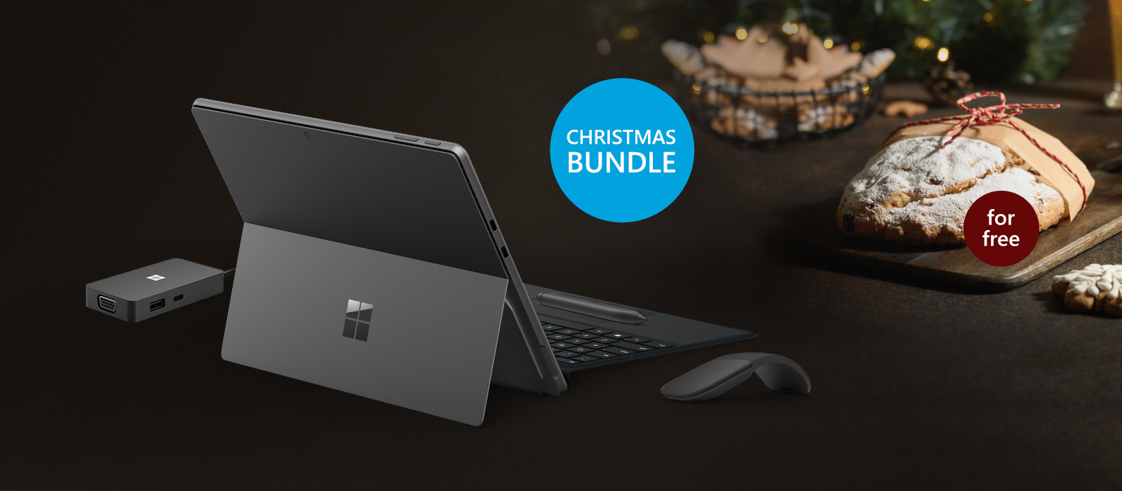 Surface Pro 9 including Surface Arc Mouse, Surface Signature Keyboard with Slim Pen 2 and Microsoft USB-C Travel Hub are shown in front of a Christmas background and a Stollen