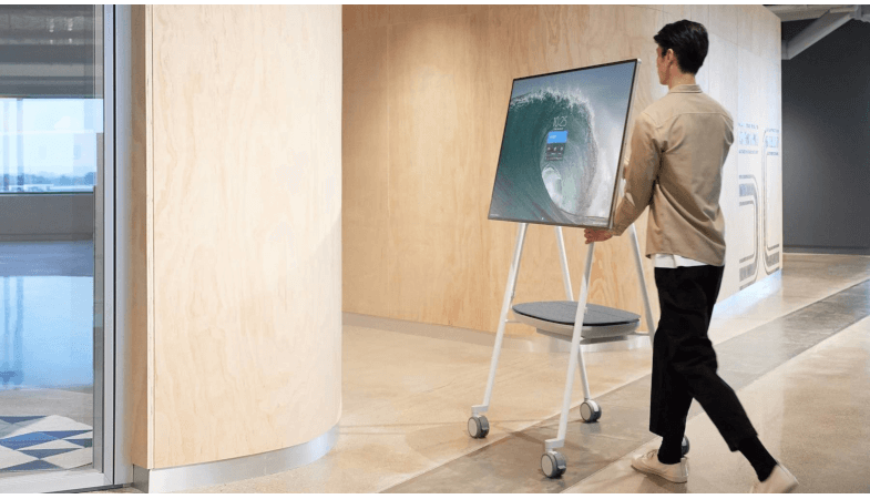 A person ist moving the Surface Hub 2S on the Steelcase Roam Mobile Stand