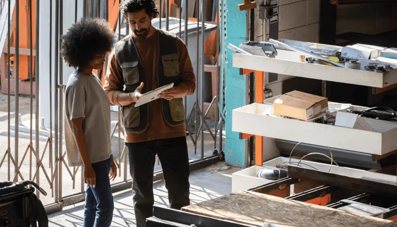 In einem Lager zeigt ein Mann einer Frau etwas auf dem Display des Surface Go 