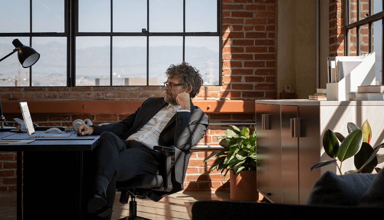 En mand sidder ved et skrivebord på et kontor og arbejder med en Surface Book 