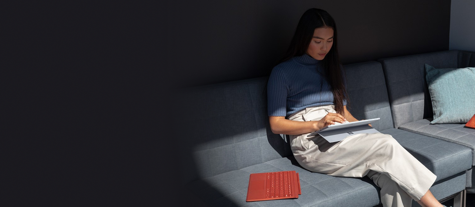 Une femme est assise sur un canapé et travaille avec le Surface Pro 7 en mode tablette