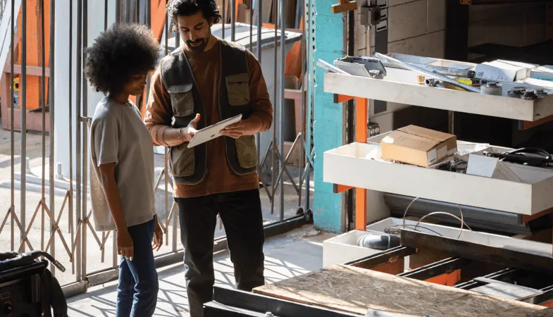 In einer Werkstatt zeigt ein Mann einer Frau etwas auf einem Surface Go 