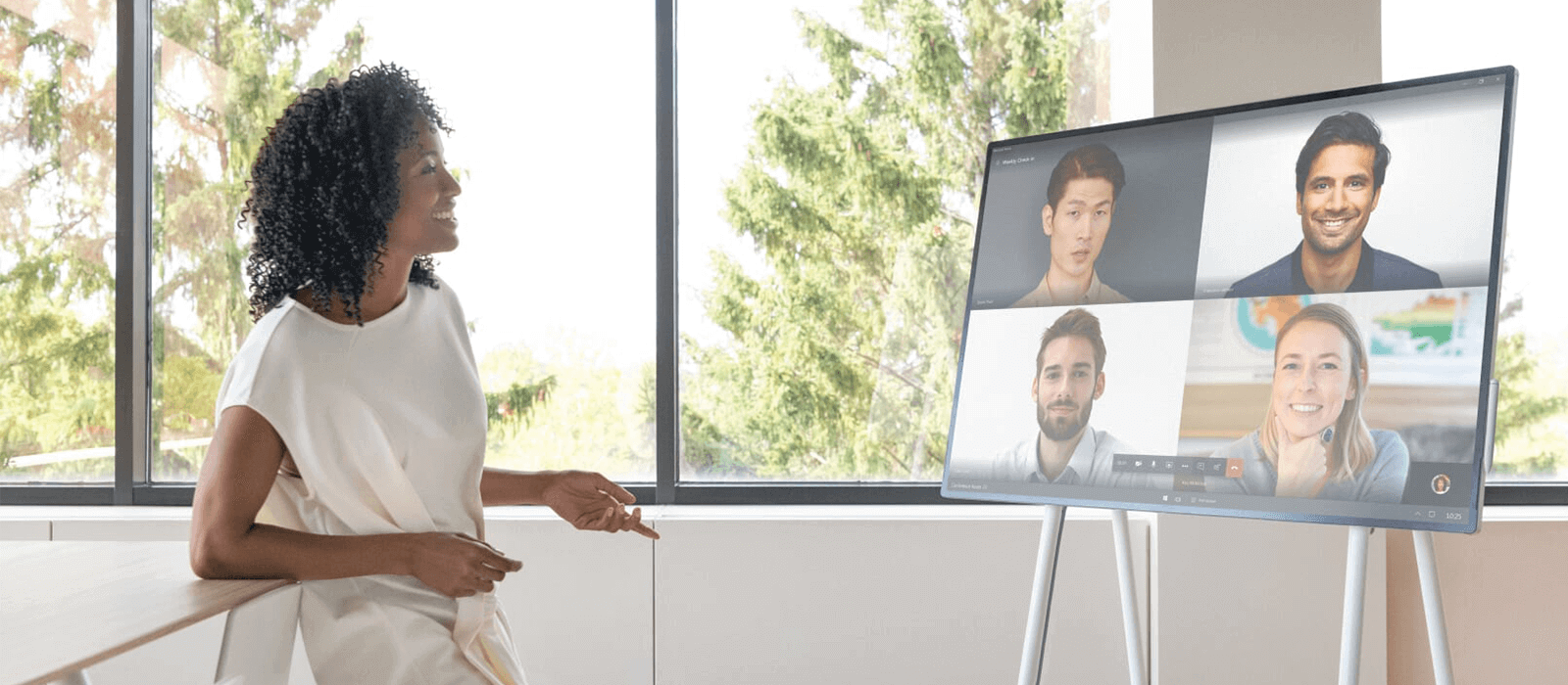A woman is standing in front of the Surface Hub 2S and is having a video conference with four people