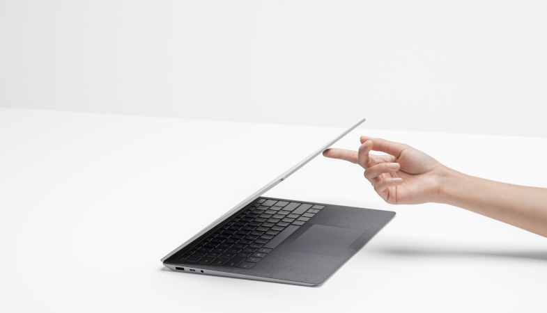 A Surface Laptop 4 stands on a white background and one persons hand opens the laptop  