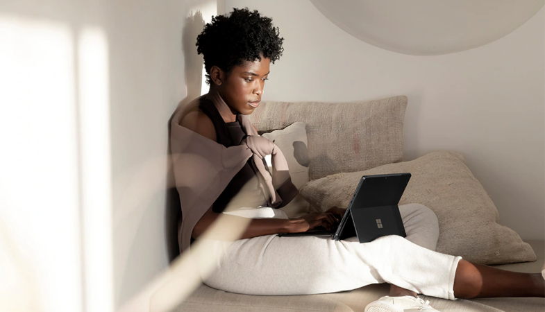 Eine Person sitzt auf einer Couch und arbeitet am Surface Pro 