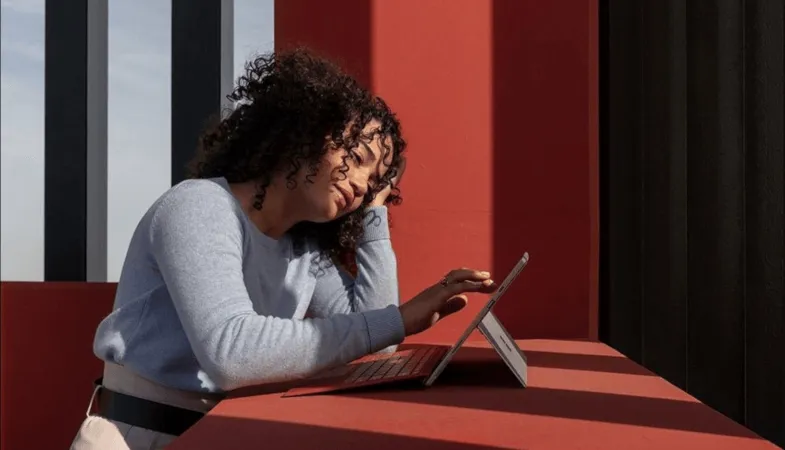 A woman sits at a table and taps her finger on the display of the Surface Pro 7