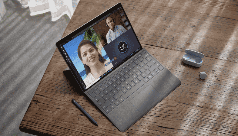 Das Surface Pro X steht zwischen dem Surface Slim Pen und den Surface Earbuds auf einem Tisch im Tablet-Modus mit Keyboard in Platin 