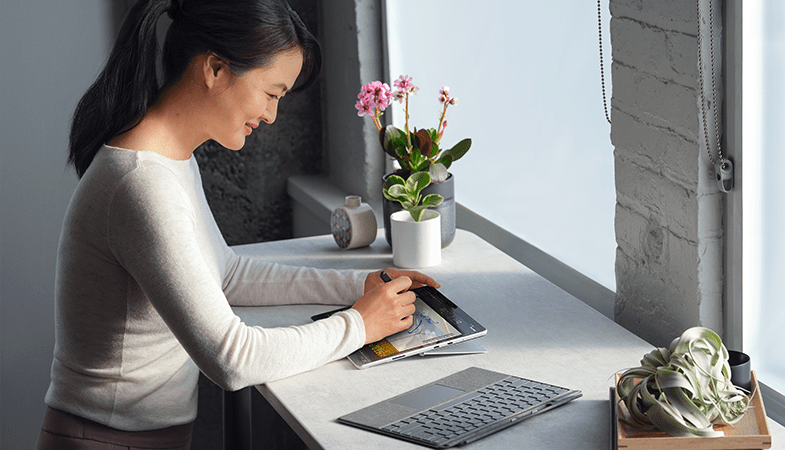 One person is working on a Surface Pro 8 with the kickstand open, next to it is the Surface Pro Signature Keyboard