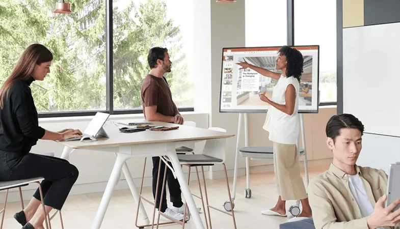 In a new work area a woman presents a PowerPoint presentation at the Surface Hub 