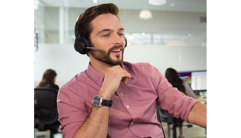 A man makes a phone call in an office with the Voyager Focus UC Microsoft headset