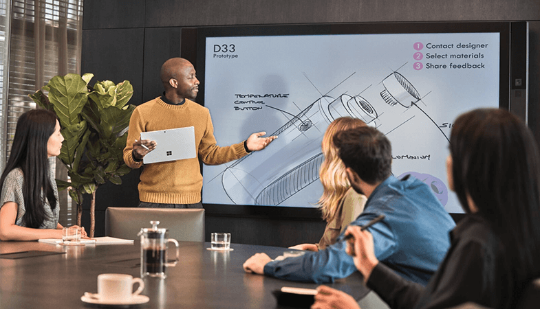 Colleagues are in a meeting, a man stands in front of a Surface Hub and gives a presentation