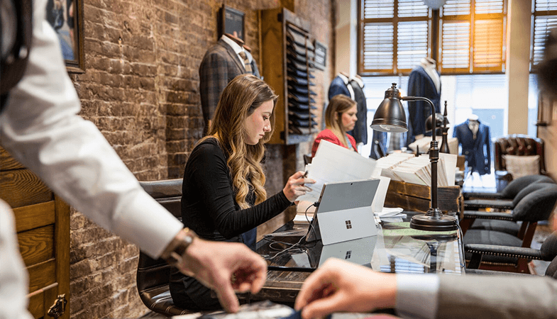 En kvinde sidder ved et skrivebord i en modebutik og arbejder på en Surface Pro