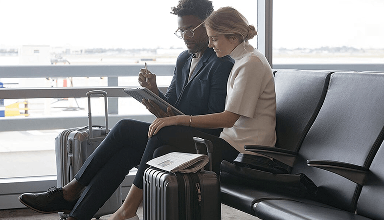 To personer sidder i lufthavnen og arbejder sammen på en Surface Pro