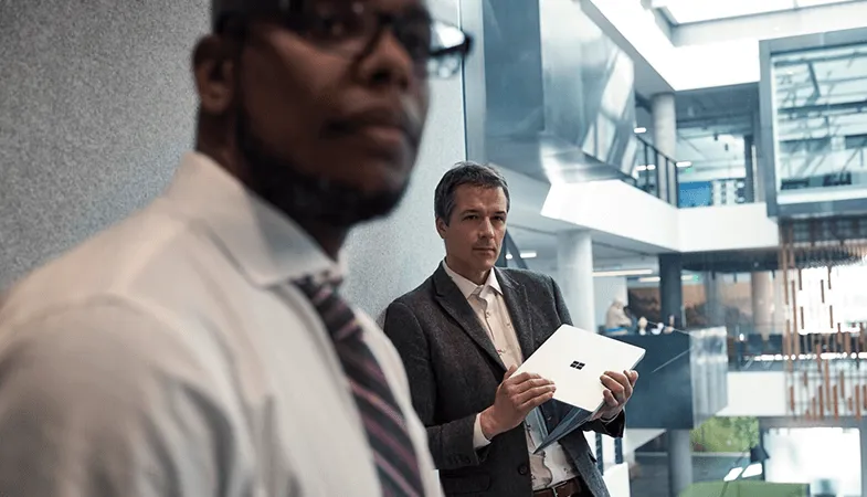 Zwei Männer stehen im Flur eines Bürogebäudes, einer hält einen Surface Laptop in der Hand 