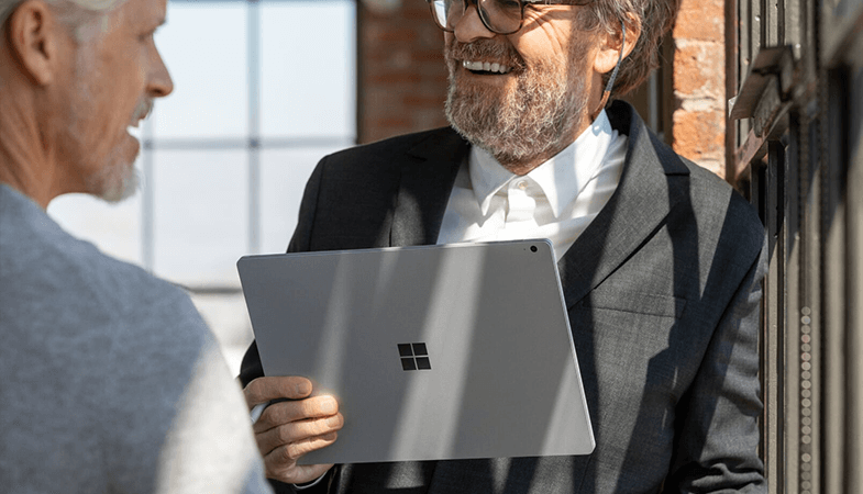 Two men are standing opposite each other, one is carrying a Surface Book in his hand  