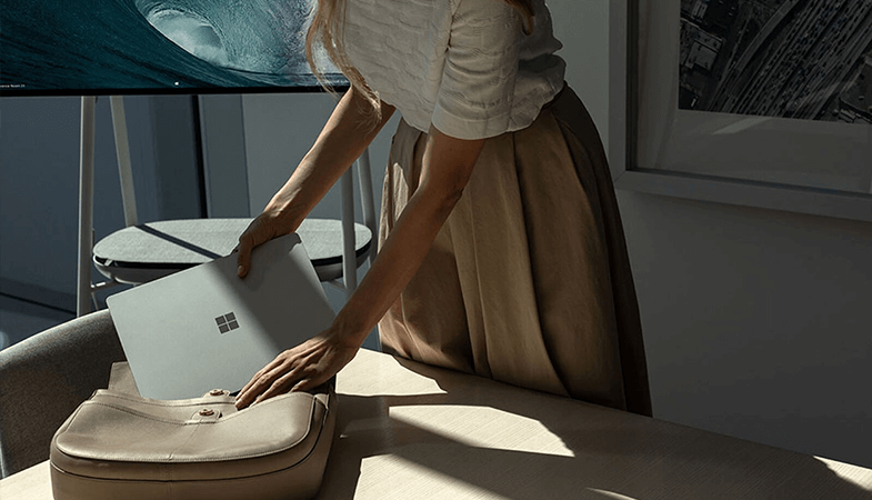 Une femme met son Surface Laptop dans son sac, qui est posé sur une table