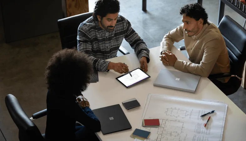 Drei Kollegen arbeiten gemeinsam am Tisch und fertigen eine Zeichnung in OneNote auf dem Surface Go an