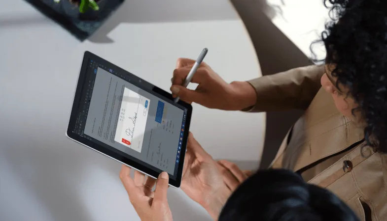 Eine Vogelperspektive zeigt den Blick auf zwei Personen, eine hält das Surface Go 4 im Tablet-Modus und die andere Person unterschreibt darauf ein Dokument mit dem Surface Pen 