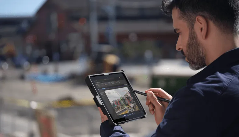 A man stands on a construction site, holding the Surface Go 3, which is framed by a protective case, in tablet mode and draws something on the display with the Surface Pen
