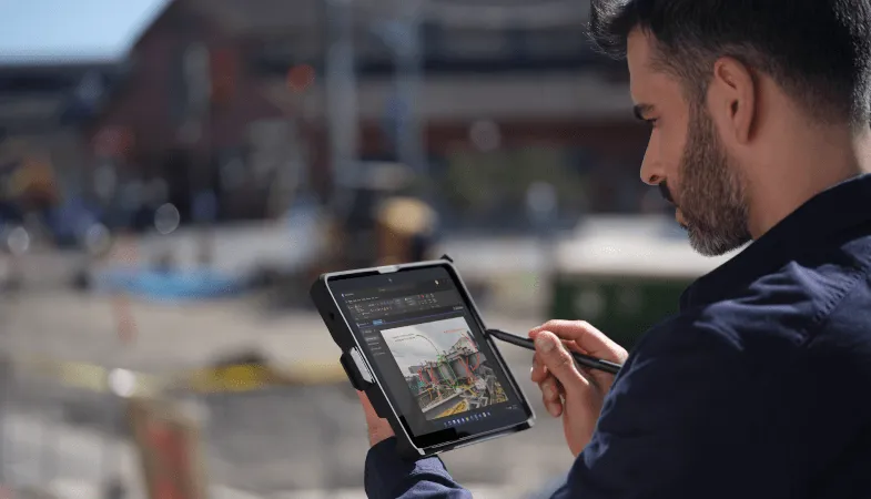 Surface Go 3 for different usage scenarios  A man stands on a construction site, holding the Surface Go 3, which is framed by a protective case, in tablet mode and draws something on the display with the Surface Pen