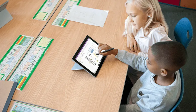 Zwei Lernende sitzen am Schultisch und arbeiten auf einem Surface Go