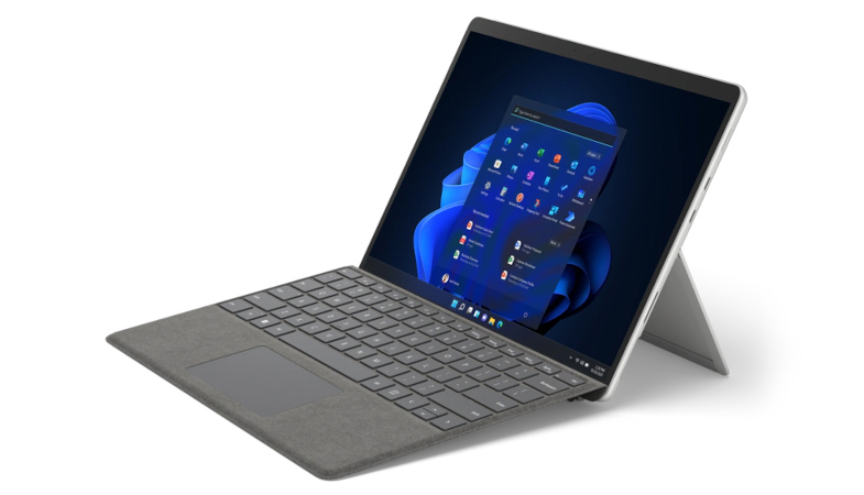 Das Surface Pro 8 in Platin aus einer seitlichen Perspektive mit Surface Pro Signature Keyboard mit blauem Herz links neben dem Surface auf dem NEU steht