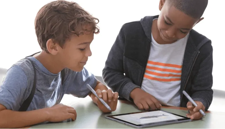 Two children use two Surface Pens to complete tasks on the Surface Go in tablet mode 