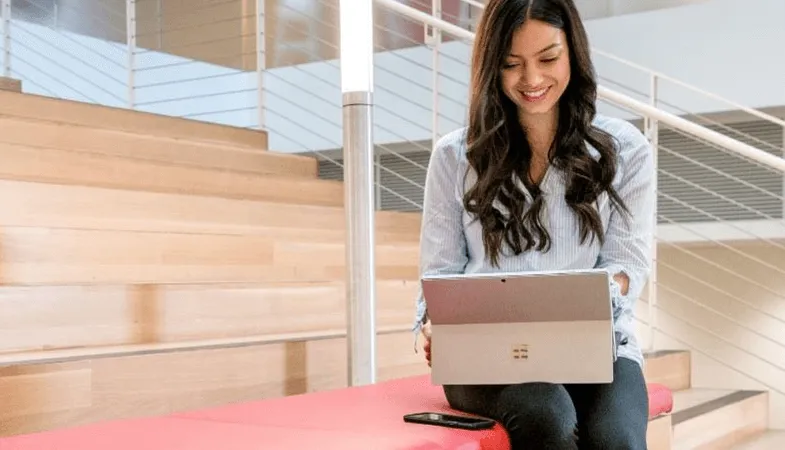 Eine ältere Schülerin sitzt auf den Treppen eines Schulgebäudes und arbeitet am Surface Pro 