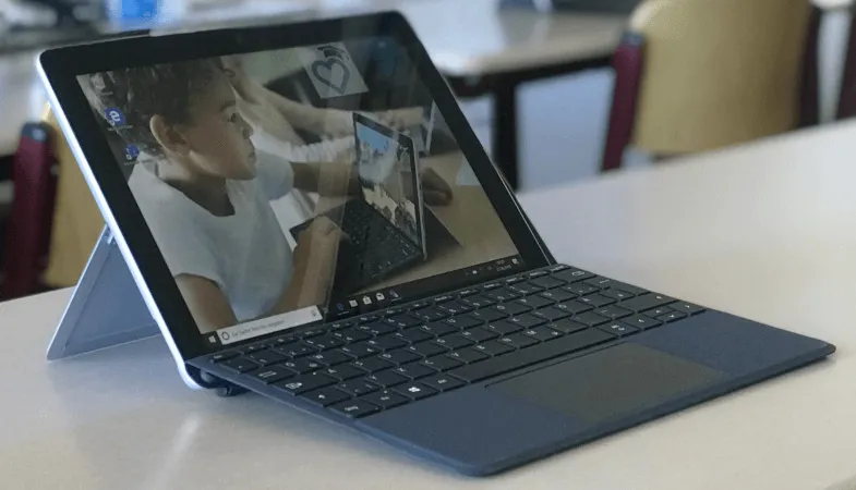 Mit Surface inklusive Zubehör und Lizenzen digital unterrichten Ein Surface Go steht im Laptop-Modus in einem Klassenraum auf einem Tisch