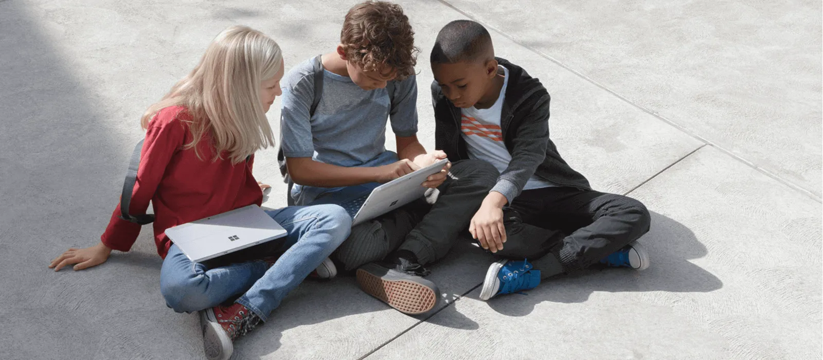 Erfahren Sie alles zum Thema digitale Schule mit Surface.Love  Drei Kinder sitzen auf dem Schulhof und schauen gemeinsam auf den Bildschirm eines Surface Go