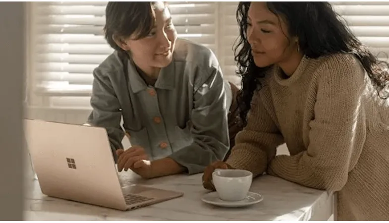 Zwei Personen sitzen nebeneinander an einem Tisch, vor ihnen steht ein Surface Laptop