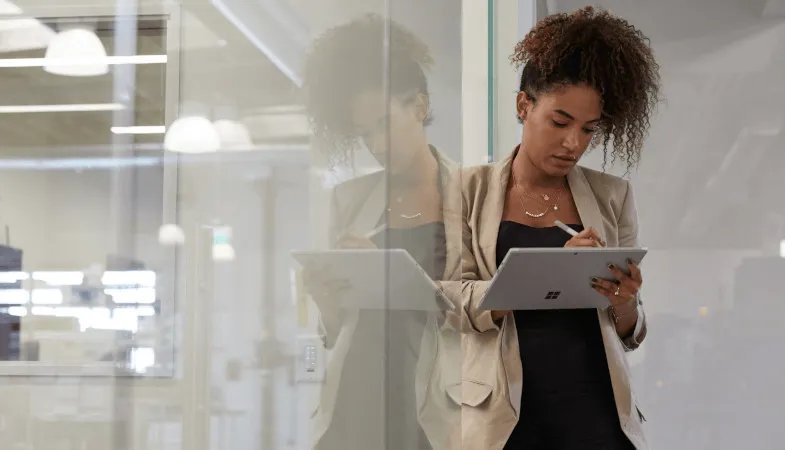 Sicherheitsfeatures schützen sensible Unternehmensdaten  Eine Frau steht angelehnt an einer Trennschreibe in einem Büro und hält das Surface Pro im Tablet-Modus in der Hand, auf dem sie mit einem Surface Pen arbeitet