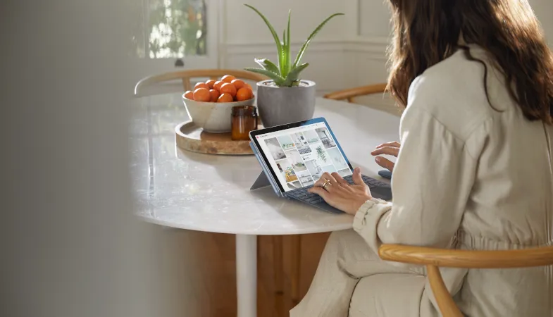 Eine Frau sitzt an einem Tisch und arbeitet auf dem Surface Go 