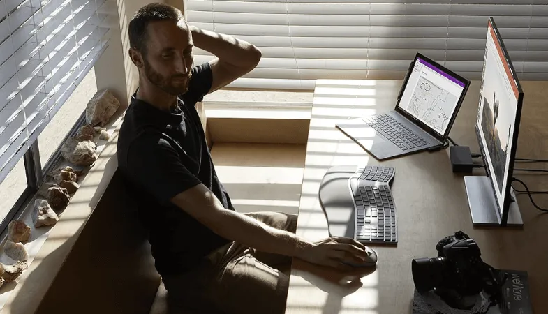 Ein Mann sitzt an einem Schreibtisch und arbeitet mit dem Surface Book sowie einem externen Monitor an einer PowerPoint-Präsentation