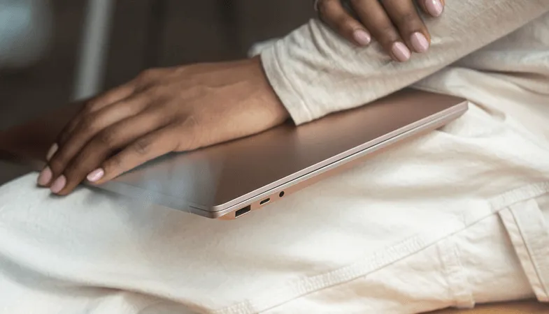 Eine Detailansicht zeigt, wie eine Frau sitzend den Surface Laptop in der Farbe Sandstein auf ihrem Bein liegend festhält 