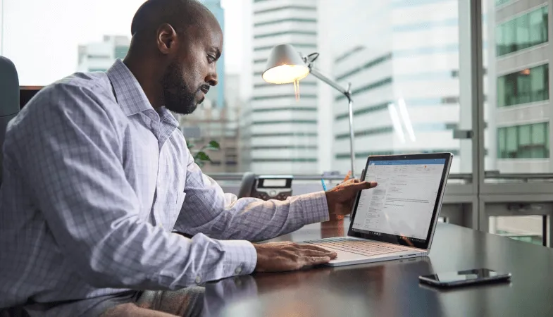 A man is sitting at a desk, in front of him stands the Surface Book with Outlook running on it 