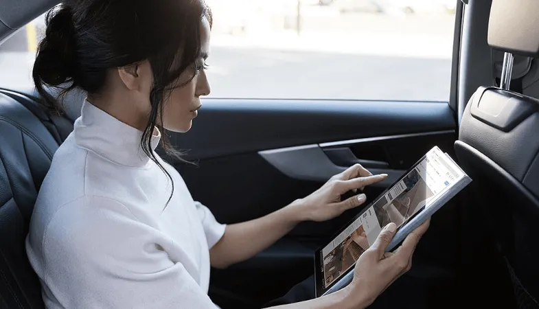 A woman sitting in the back seat of a car and working on the Surface Pro in tablet mode 