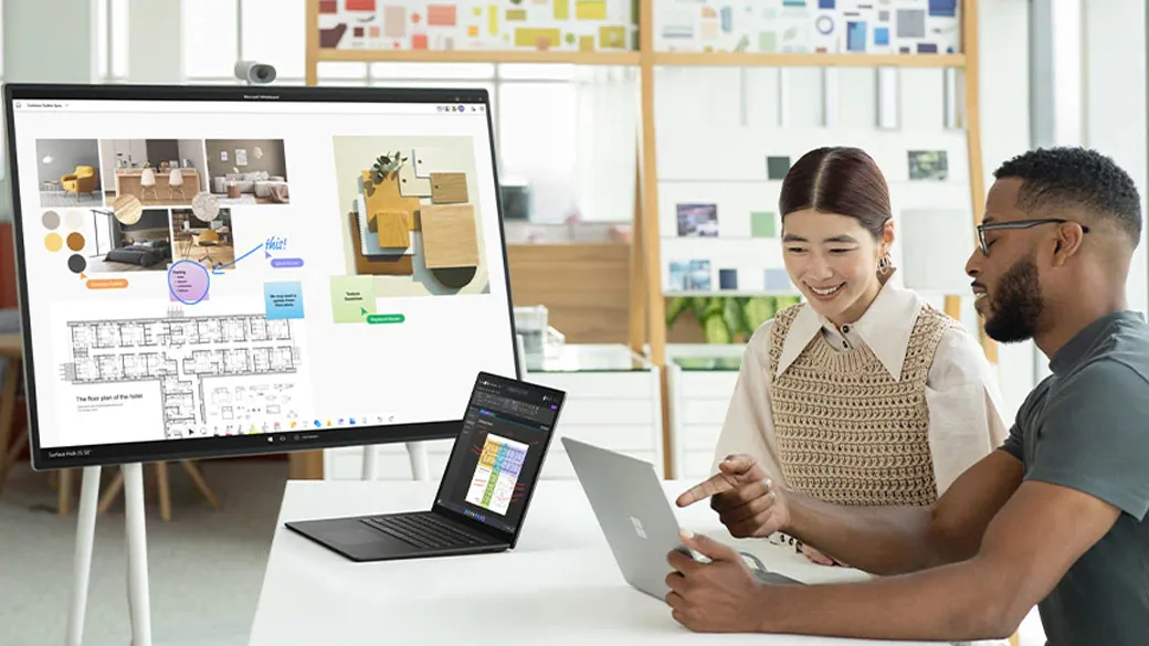 Ein Mann und eine Frau arbeiten zusammen an einem Surface Laptop 5 der mit einem Surface Hub 2S verbunden ist