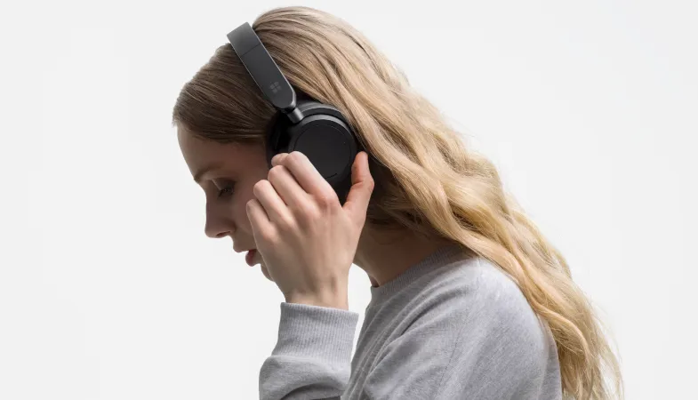 A woman wears the Surface Headphones 2 Plus on her head and touches an on-ear dial