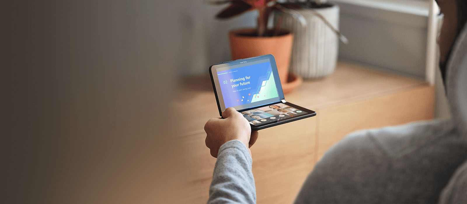 Eine Person sitzt an einem Schreibtisch und hält das Surface Duo 2 in der Hand