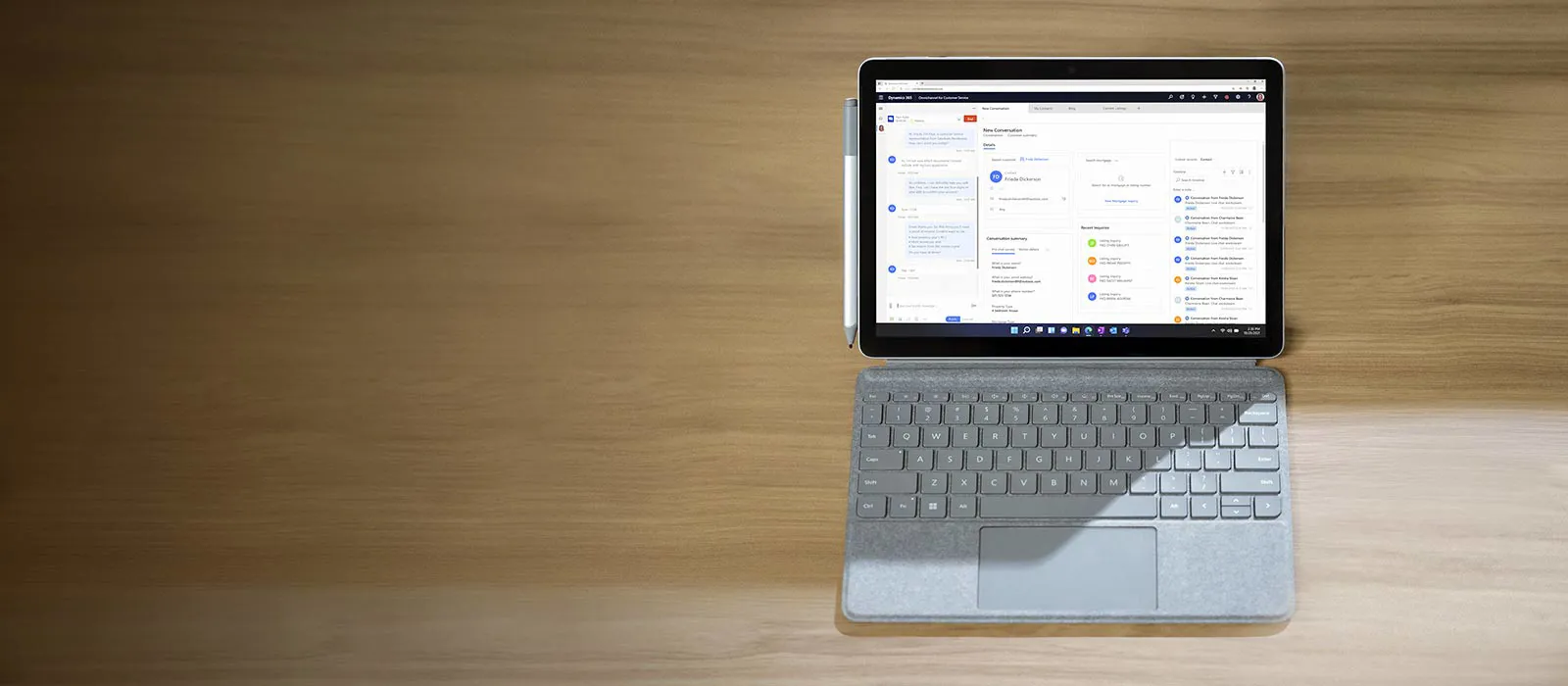 A Surface Go 4 is standing on a wooden surface in laptop mode, with the Dynamics 365 application open on the Surface screen