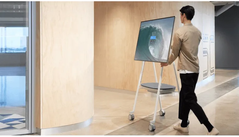 Das Surface Hub 2S mit dem Steelcase Roam Rollständer leicht bewegen können Eine Person schiebt das Surface Hub 2S auf dem Steelcase Roam Rollständer