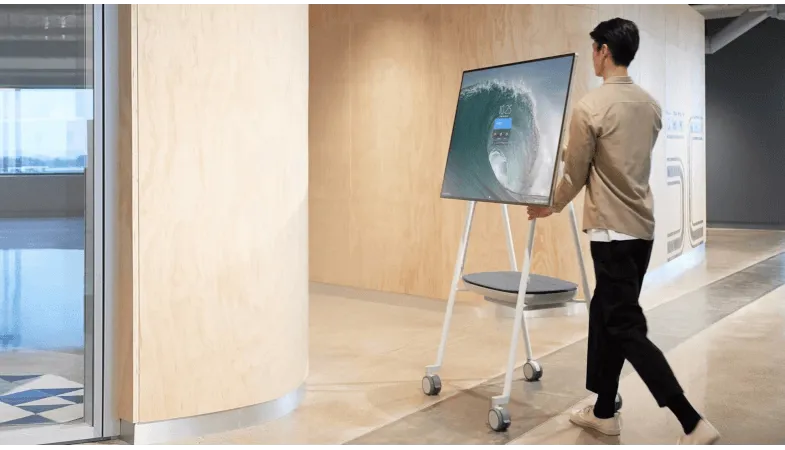 A person is moving the Surface Hub 2S on the The Steelcase Roam Mobile Stand