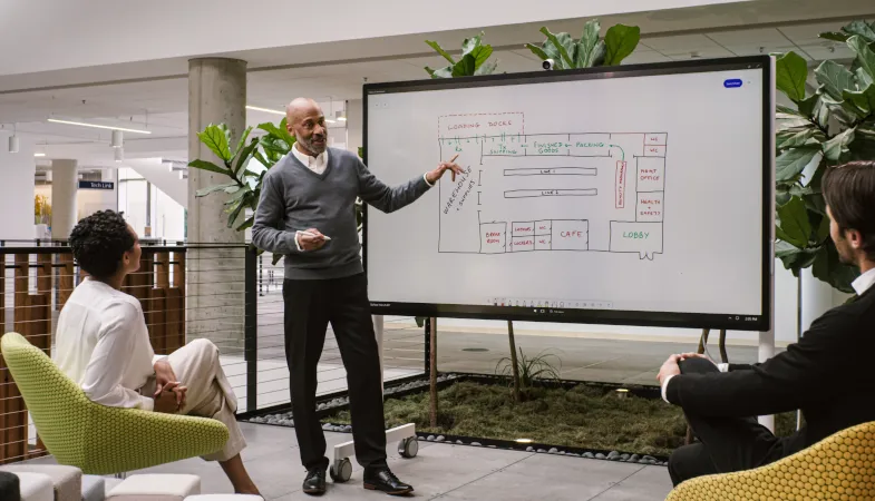 Eine Person präsentiert anderen Personen etwas am Surface Hub 2S 85 Zoll in einer modernen Büroumgebung 