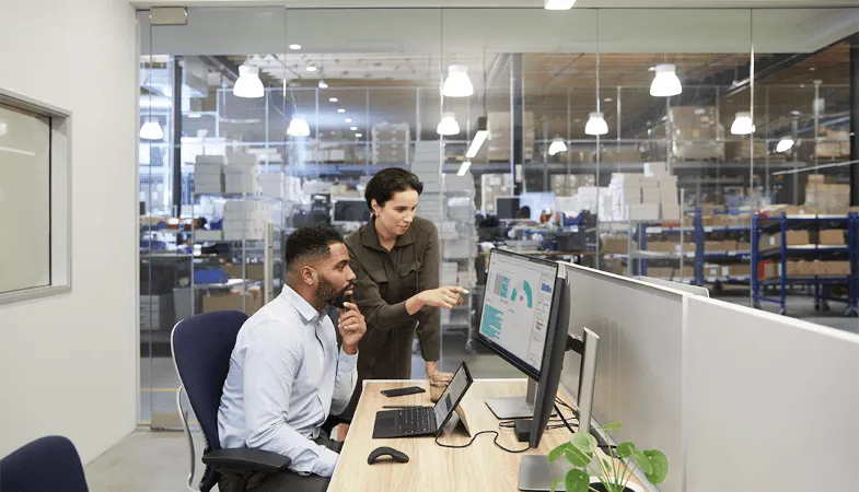 In an office, a woman explains a graphic on the monitor to a man 