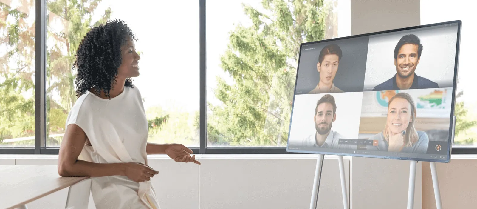 Eine Frau steht vor einem Surface Hub 3 und hält eine Videokonferenz mit vier Personen