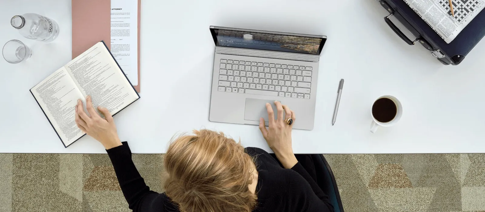 Vogelperspektive auf einen Schreibtisch, an dem eine Frau mit dem Surface Book arbeitet