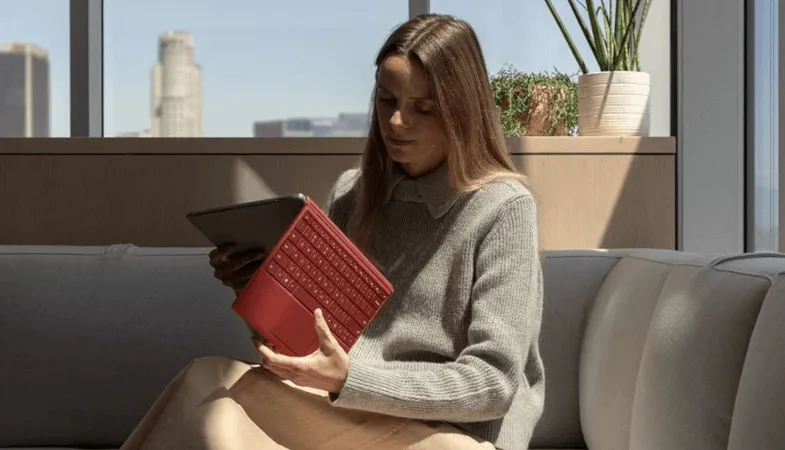 Eine Frau sitzt auf einem Sofa und klappt das Signature Type Cover des Surface Pro 7 zurück